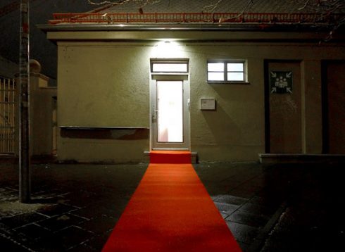 Nächtliche Außenansicht von Das KloHäuschen, ein roter Teppich führt vom Gehweg bis zum hell beleuchteten Eingang.