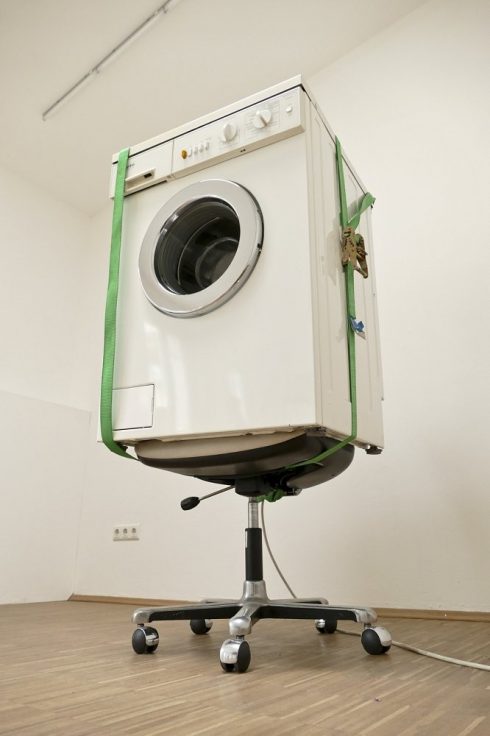 Waschmaschine mit grünen Gurten auf einem Bürostuhl in einem leeren Raum.