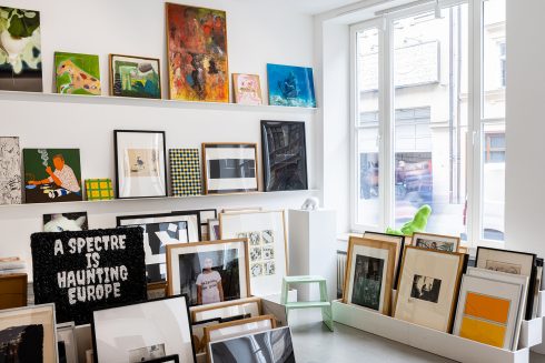 Innenraum der Artothek mit gerahmten Kunstwerken auf Regalen und Stellflächen nahe eines großen Fensters.