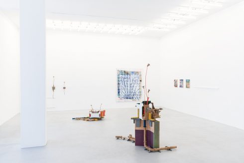Heller Ausstellungsraum mit skulpturalen Arbeiten auf dem Boden und Wandarbeiten im Hintergrund.