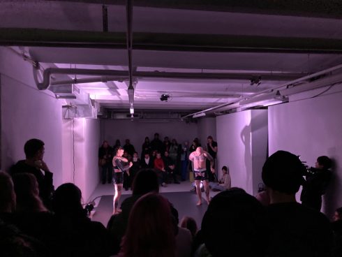 Performance in einem Ausstellungsraum mit zwei Tänzer*innen und Publikum unter violettem Licht