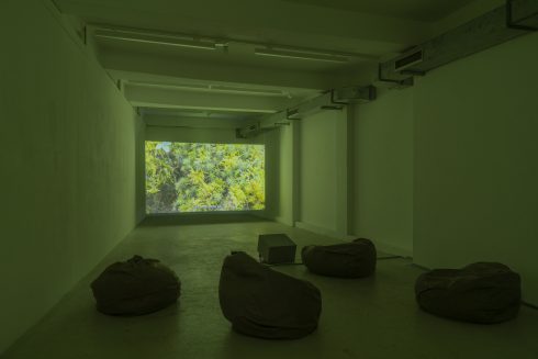Abgedunkelter Raum mit Videoprojektion an der Stirnwand und Sitzsäcken auf dem Boden.