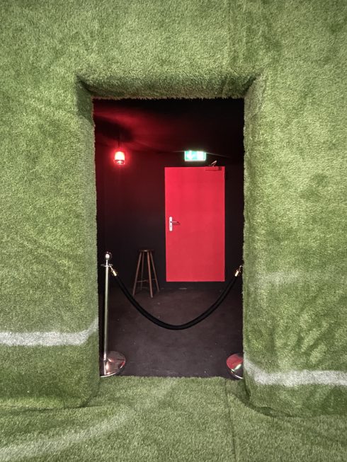 Grün ausgekleideter Durchgang mit roter Tür, Absperrband und Notausgangsschild.