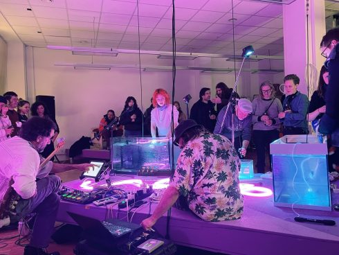 Audiovisuelle Live-Performance mit Musiker*innen und leuchtenden Wasserbecken, umgeben von einem stehenden Publikum.